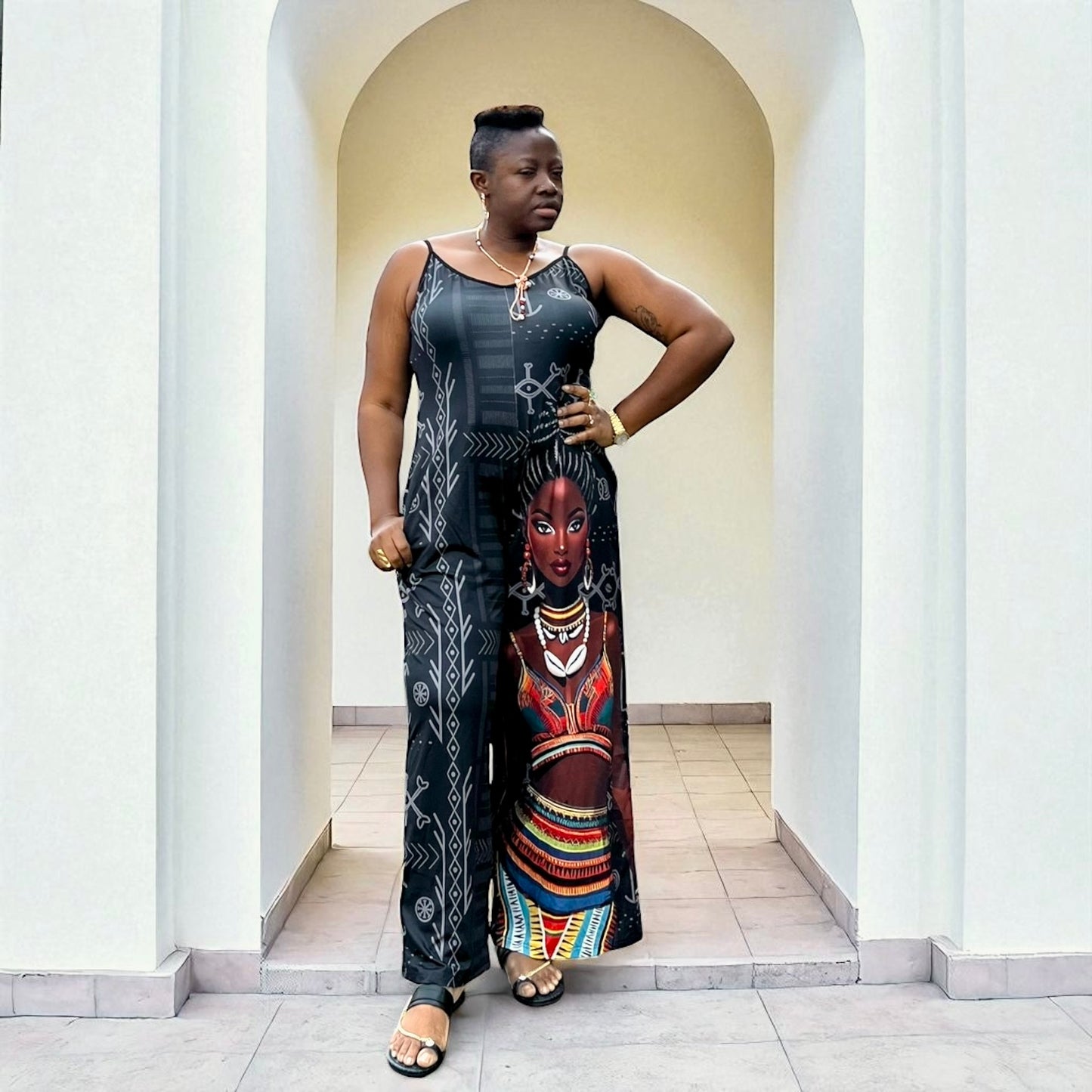 Woman wearing a long, patterned jumpsuit standing in an archway.