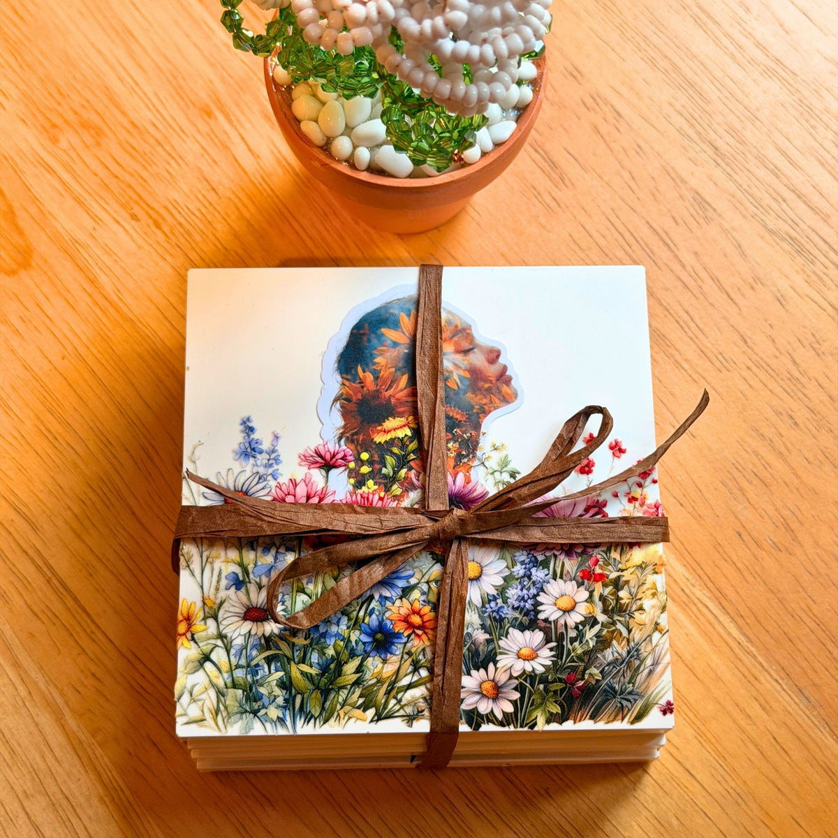 Set of four Nature Within Women & Flowers coasters stacked and tied with brown ribbon, featuring colourful floral portrait illustrations.